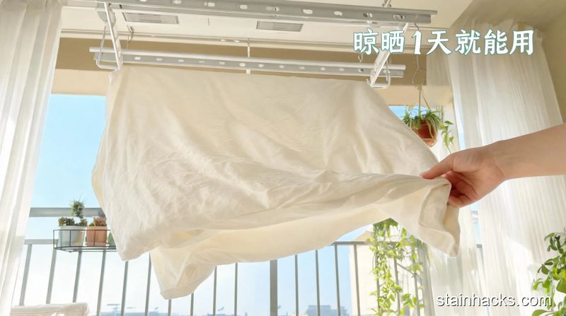 阳台晾衣架区域场景,平铺在晾衣架上的纯棉床单,人手轻轻调整拉伸床单边角的动作,配有文字「晾晒1天就能用」,风格清新明亮生活化,关键元素:方便、省时间